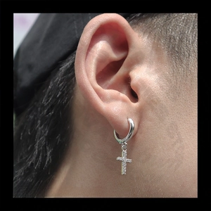 Close-up of silver hoop earring with iced out cross pendant featuring cubic zirconia