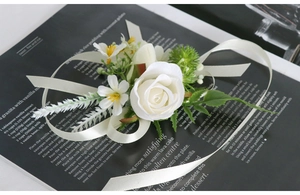 Detail of white artificial rose boutonniere with satin ribbon and green leaf accents
