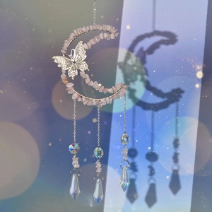 Detail of moon-shaped suncatcher with pink crystals and butterfly ornament in soft light