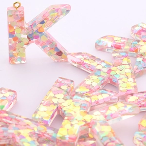 Macro shot of pink resin letter K keychain with colorful heart sequins and gold ring