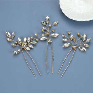 Detailed view of three gold hair pins with sparkling clear crystal leaves on blue backdrop