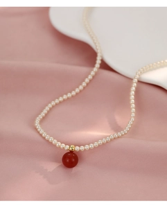 Détail d'un collier de perles avec perle dorée et pendentif en agate rouge sur soie
