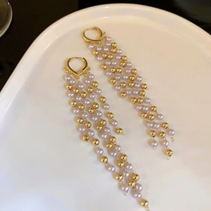 Close-up of gold dangle earrings with lilac pearls and long bead tassels on white plate