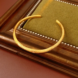 Close-up of a brushed gold open bangle with gem accents on a vintage green fabric pad