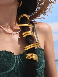 Outdoor close-up of golden geometric hair rings styled on a model by the sea