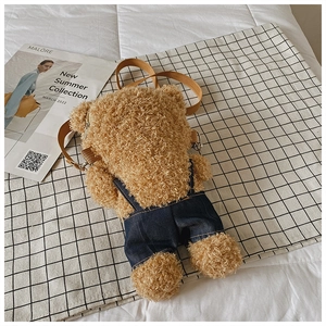 Detail of cute plush teddy bear bag in denim overalls on cozy white bedding