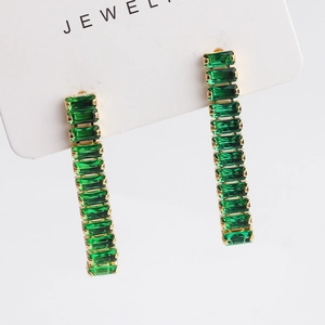 Elegant gold drop earrings with linear rectangular green zircons on a white display card