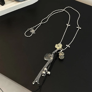 Detailed close-up of a silver chain necklace with heart pendant, spotted stone, and fringe tassel