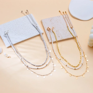Détail de colliers superposés en or et argent avec perles blanches et disques ciselés