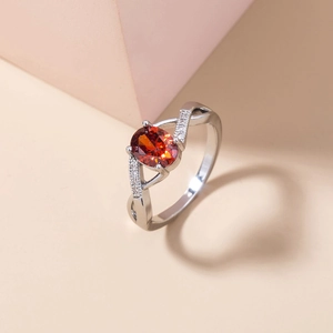 Macro detail of oval red gemstone ring with clear zircon accents on silver band