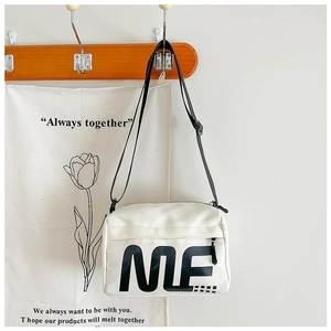 Gros plan du sac bandoulière en toile blanche avec lettrage ME noir et sangle
