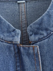 Detail of blue denim jacket collar featuring contrast orange stitching and twill texture