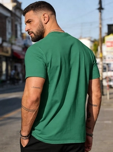 Outdoor street view of the back of a men's forest green cotton crewneck T-shirt