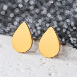 Macro shot of minimalist teardrop gold earrings on a textured white stone surface