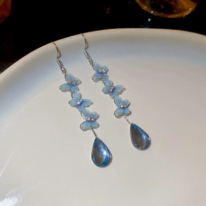 Close-up of blue matte flower drop earrings with a crystal pendant on ceramic tray
