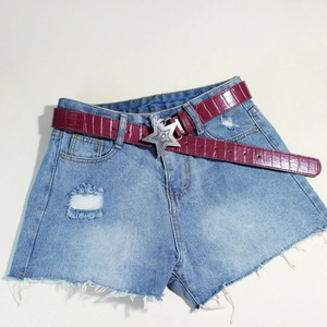 Detail der sternförmigen Silberschnalle an einem dunkelroten Krokodilledergürtel mit Denim