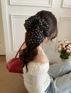 Detail of a large chiffon bow hair claw with white floral pattern on black fabric