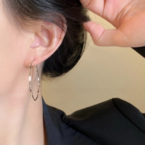 Close-up of large silver hoop earrings with hammered texture worn by a model