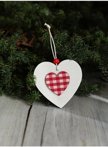 Detail of wooden heart ornament with red gingham fabric and white bead on pine background