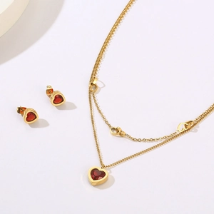Detail of double-layer gold necklace and matching red heart-shaped earrings on white background