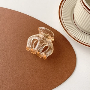 Detailed view of an amber acrylic hair claw clip resting on a textured leather surface