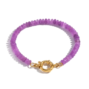 Detailed macro view of purple-red beaded bracelet with golden spring clasp on white background