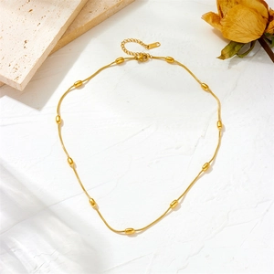 Minimalist gold stainless steel beaded necklace with oval grains on a beige travertine base