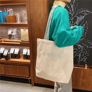 Detail of off-white corduroy tote with Smile embroidery and bohemian pom-pom strap