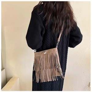 Detail of a brown suede crossbody bag featuring long fringes and a round metal button