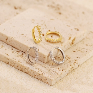 Detailed close-up of geometric gold and silver hoop earrings with clear zirconia stones