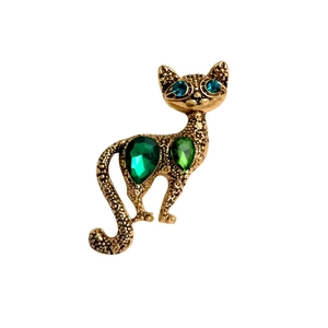 Vintage gold cat brooch with green crystals and floral engraved details on white background