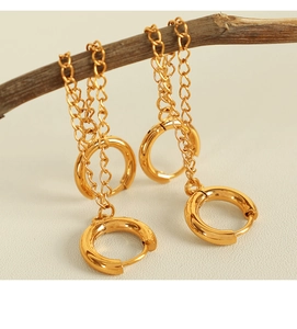 Elegant gold drop chain earrings hanging on a rustic branch against leather background