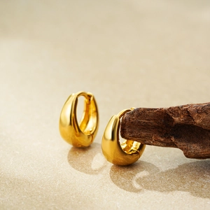 Classic 18K gold plated teardrop hoop earrings displayed on dark wood with textured background