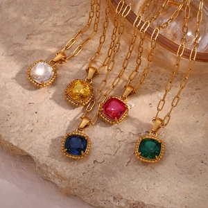 Golden paperclip chain necklaces with colorful square gemstone pendants on stone