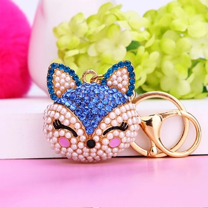 Detailed view of fox head keychain with blue rhinestones and white pearls on gold metal