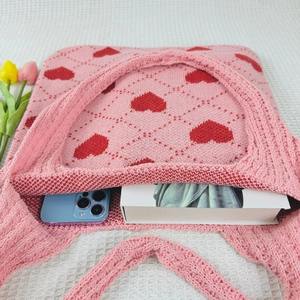 Detailed capacity of pink knitted tote bag with red hearts showing phone and book inside