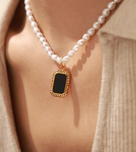 Close-up of pearl necklace with a black rectangular pendant set in gold on a model