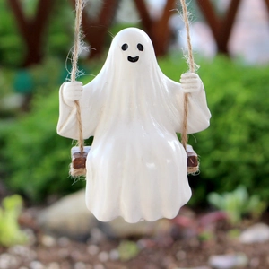 Detailed view of a cute white ghost figurine sitting on a wooden swing with hemp rope