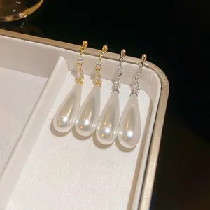Water-drop pearl earrings with gold and silver frames on textured beige jewelry box