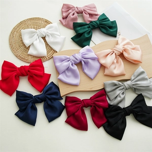 Flat lay of ten colorful satin bow hair clips in multiple shades on an elegant beige surface