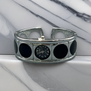 Detailed macro view of silver bangle watch with black rectangular dial on marble background