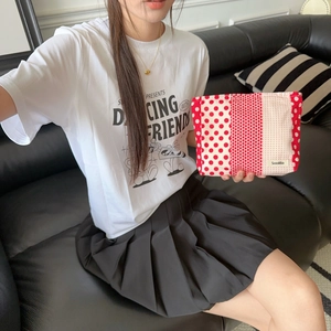 Floral makeup bag with red dots being held by a model on a leather sofa