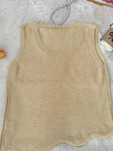 Detail van lichtgouden gebreide vest met pailletten, geschulpte zoom en fijne textuur
