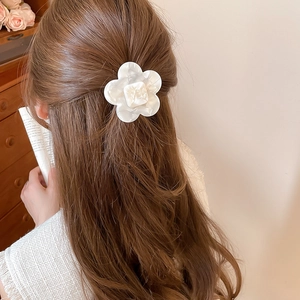 Detailed side view of a white resin flower hair clip with pearlescent finish on brown hair