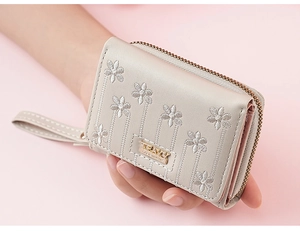 Close-up of beige wallet featuring elegant floral embroidery and metal zipper detail