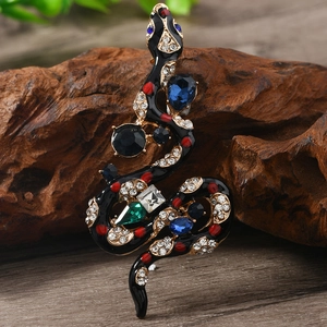 Vintage snake brooch in gold alloy with colorful crystals on a rustic wood background