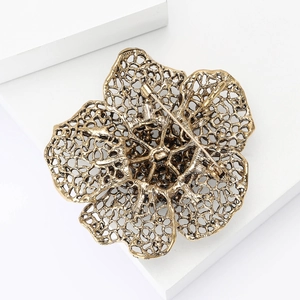 Detail of vintage gold flower brooch with hollow design on a white geometric stand