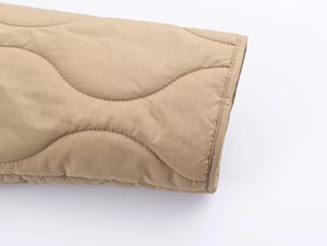 Détail de la manche matelassée kaki avec coutures ondulées et texture quadrillée ripstop