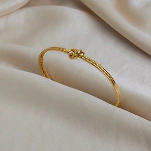 Bracelet jonc ouvert doré 18 carats avec design nœud élégant sur fond de soie luxueux