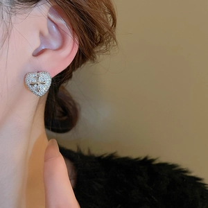 Close-up of heart-shaped earring with cross design and zircon inlay on model's ear